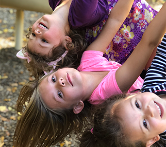 Three female students hang from a jungle gym