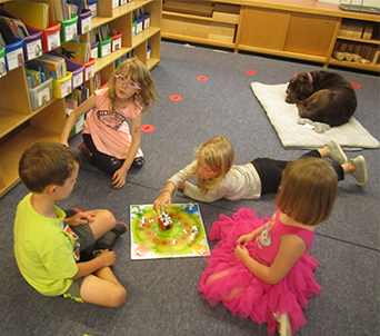 Four students play a game in a library and a dog sleeps nearby